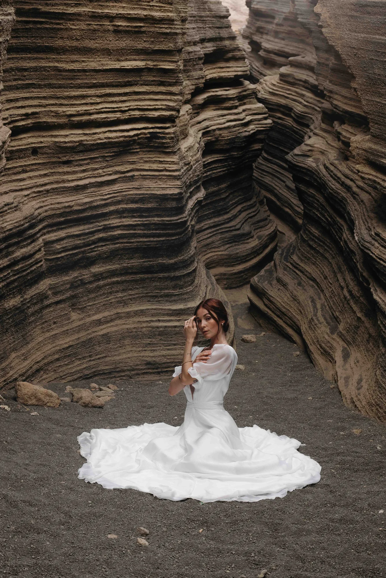 Mariée assise au fond d’un canyon, la jupe de la robe 02 de la capsule Meltem étalée en corolle