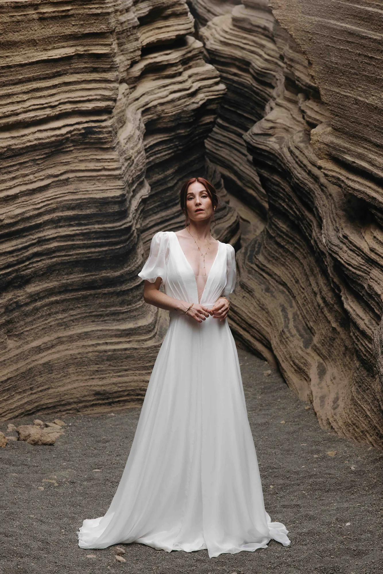 Robe 02 de la capsule Meltem en mousseline de soie portée de face dans un canyon de roche, décolleté plongeant et manches ballon